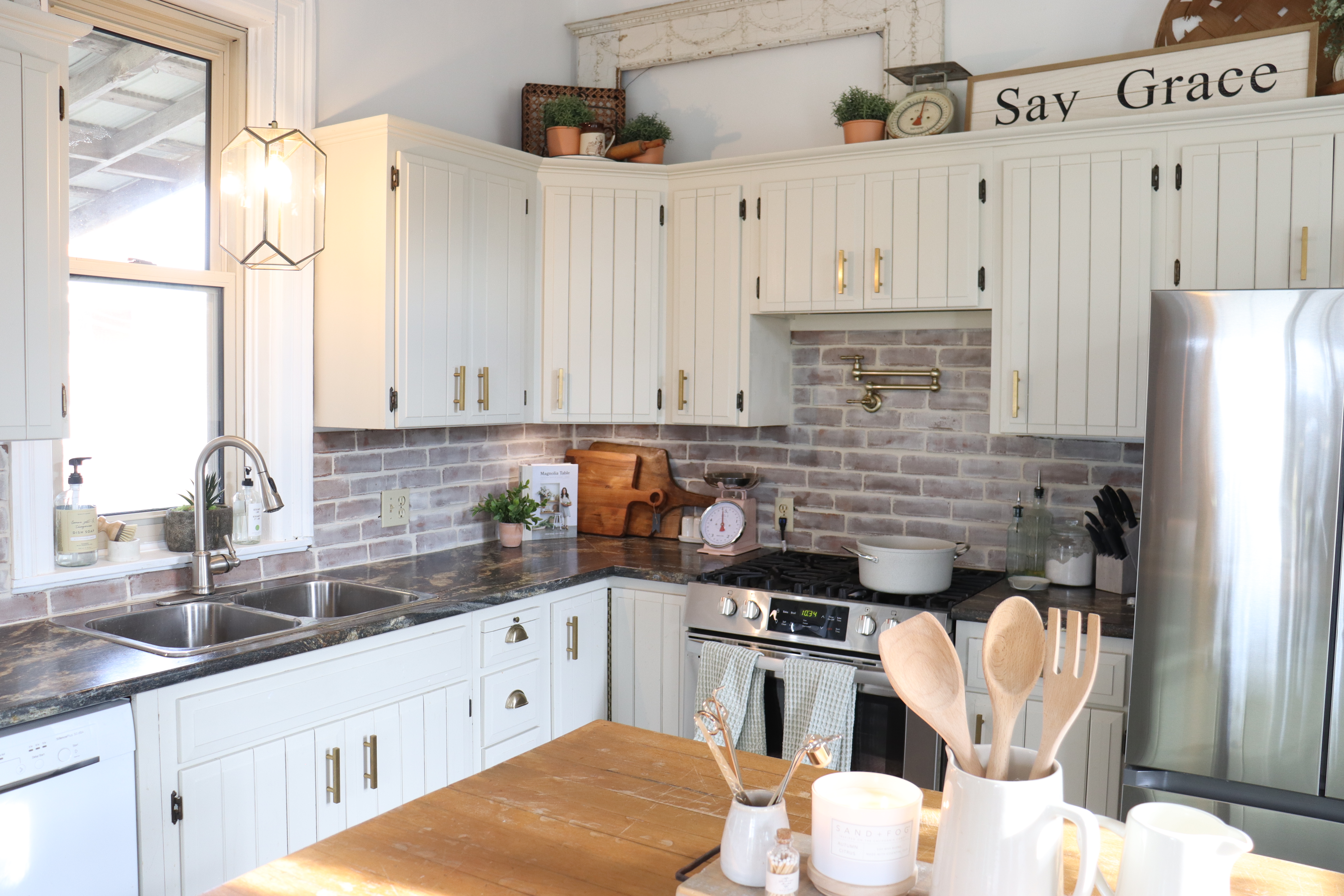 country kitchen with brick backsplash cream cabinets gold pot filler say grace sign farmhouse style
