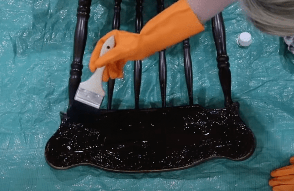 woman wearing orange gloves applying paint stripper to head of antique chair